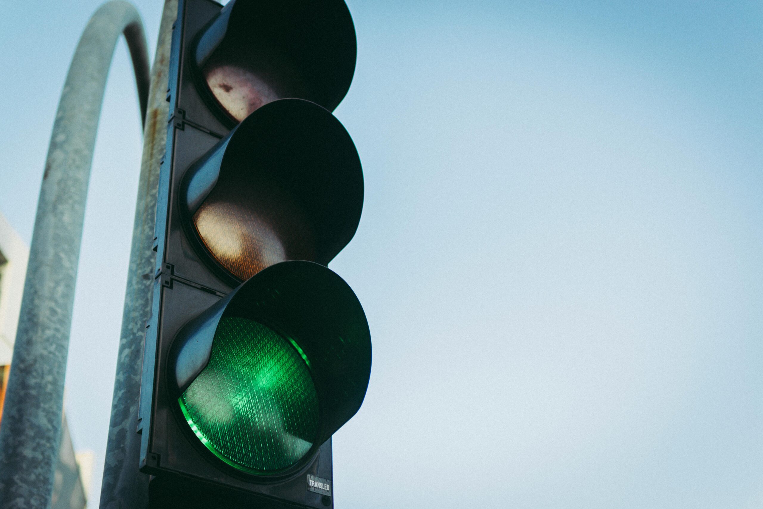Close-up of a green traffic light against a clear blue sky, symbolizing go and safety.